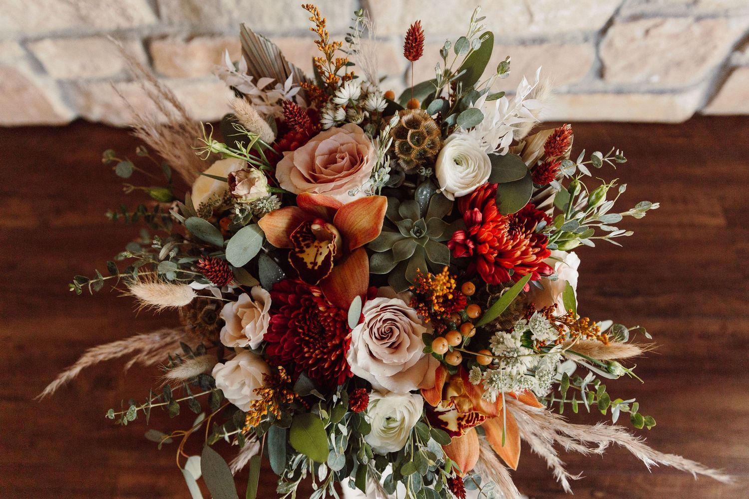 Romantic fall wedding bouquet with pink roses, red berries, and mixed greenery on wooden surface.
