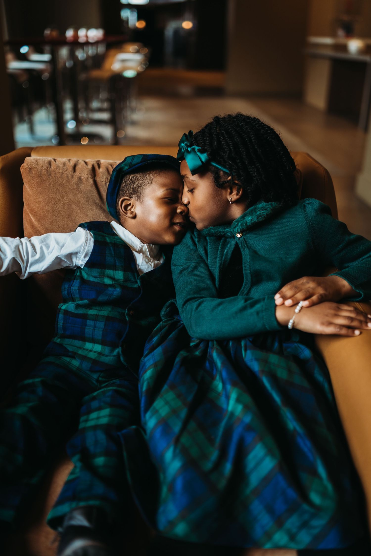 Children in matching plaid outfits cuddling together in dim lighting.