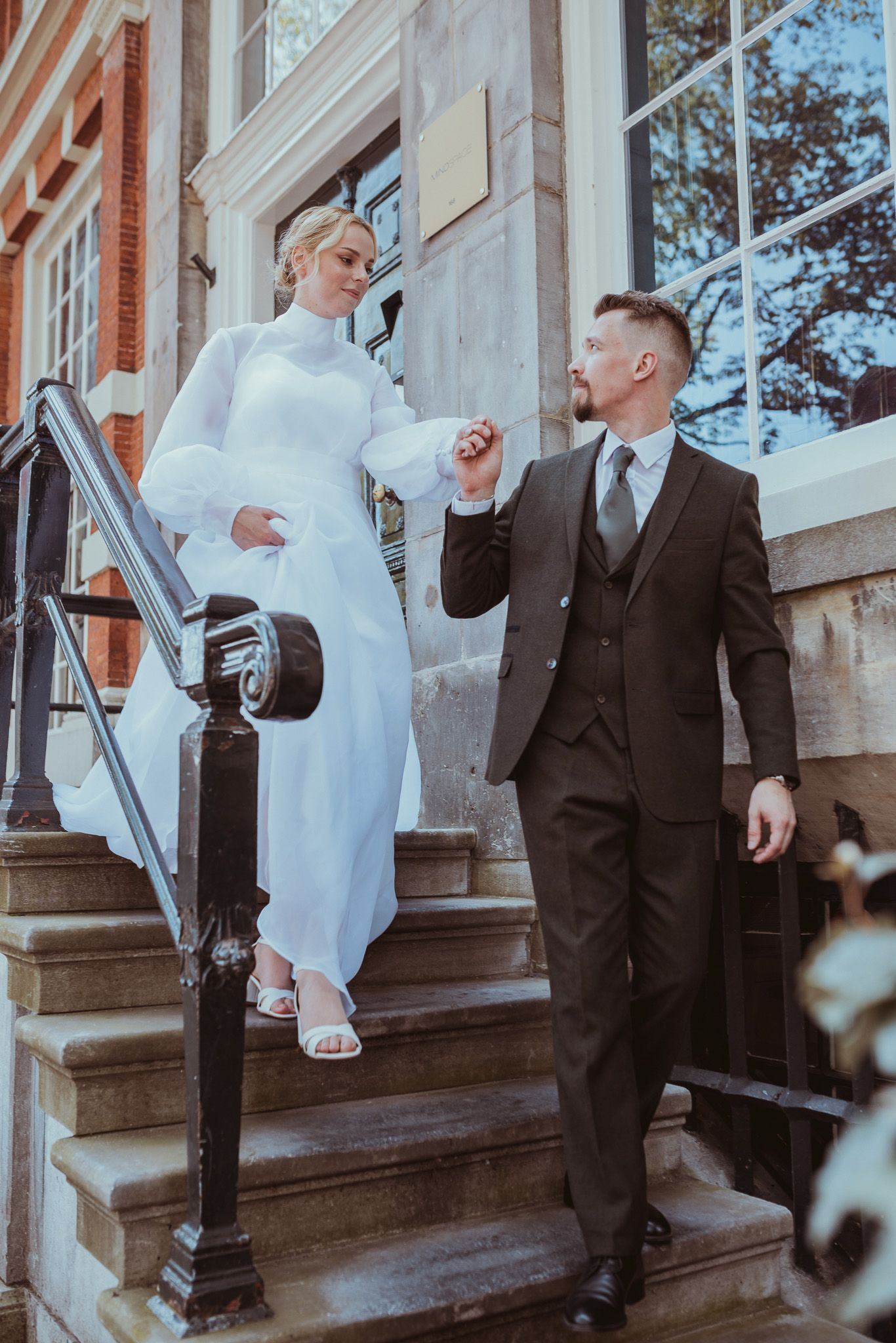 A couple in wedding attire share a playful moment on the steps of historic building in Amsterdam.