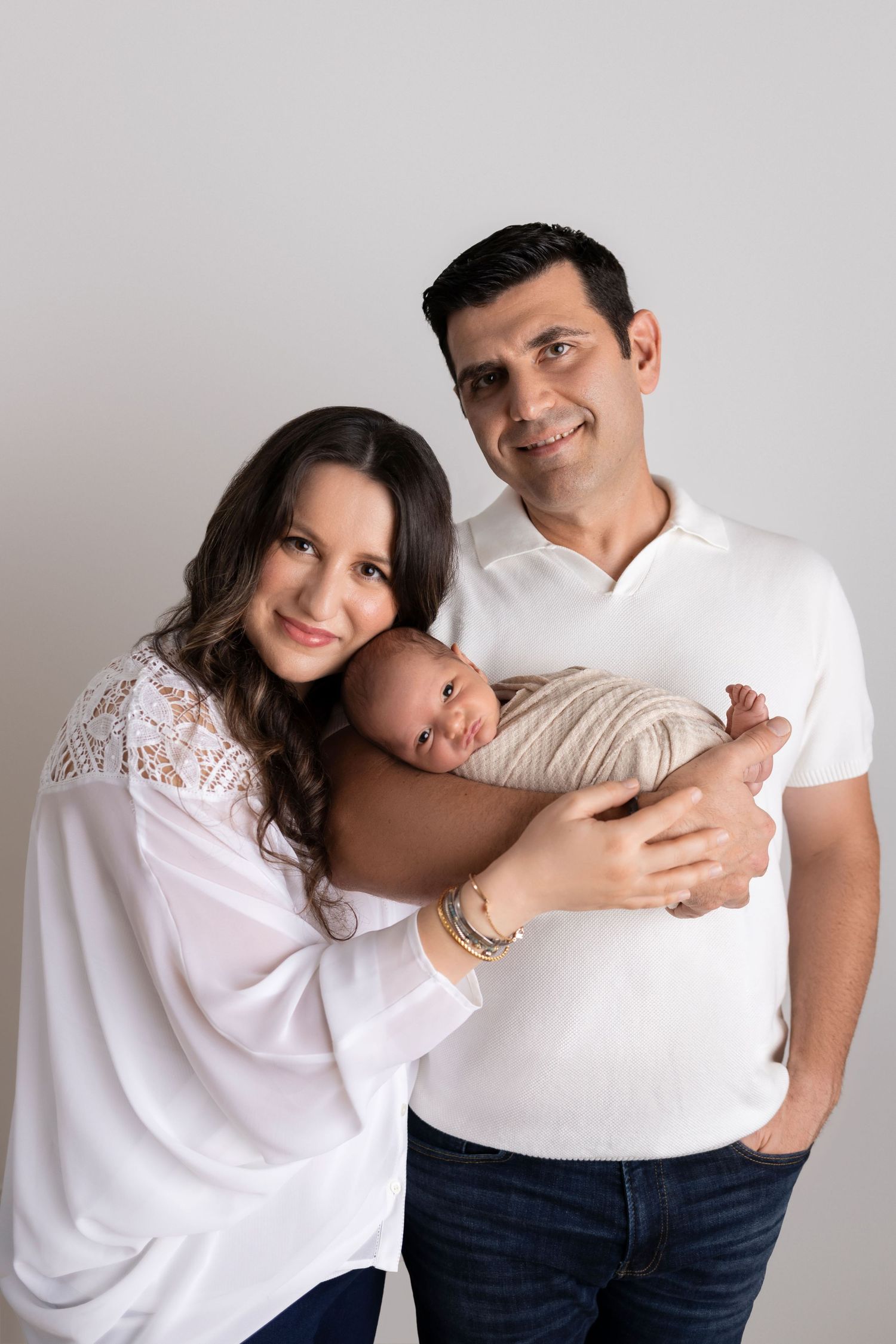 A couple wearing white tops poses together in a series of affectionate studio portraits against a light gray background.