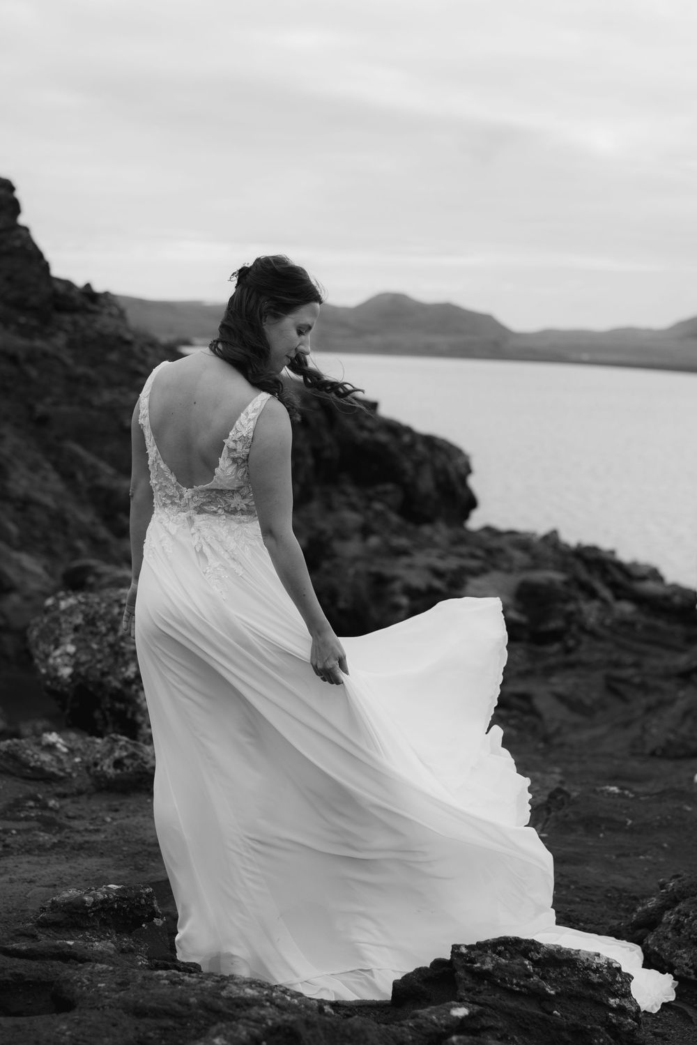 Bride standing at the shore of Kleifarvatn Lake with wind blowing her dress