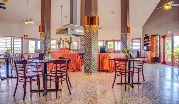 Modern dining area with orange accents, patterned columns and high ceilings in resort setting.