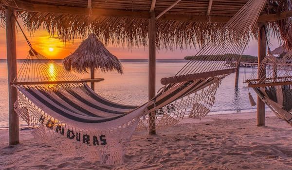 Hammock on beach at sunset with thatched palapa and Honduras sign.
