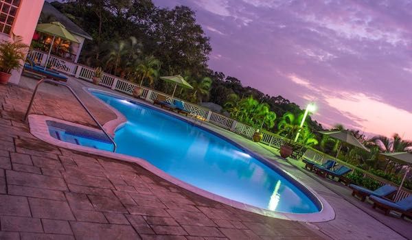 Illuminated swimming pool with curved edges glows under a dramatic purple sunset sky.
