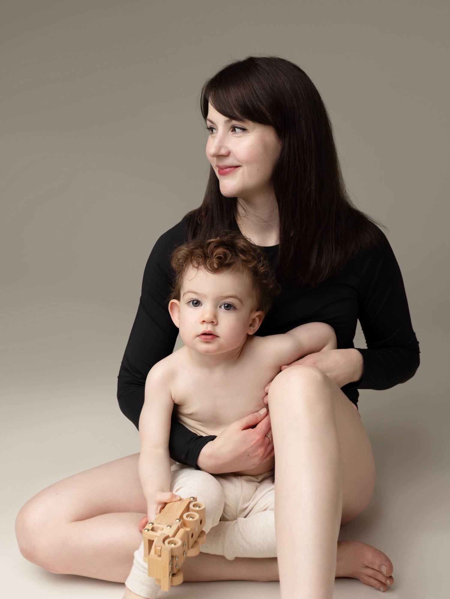 A series of intimate portraits showing a mother in black clothing holding a baby against a neutral studio backdrop.