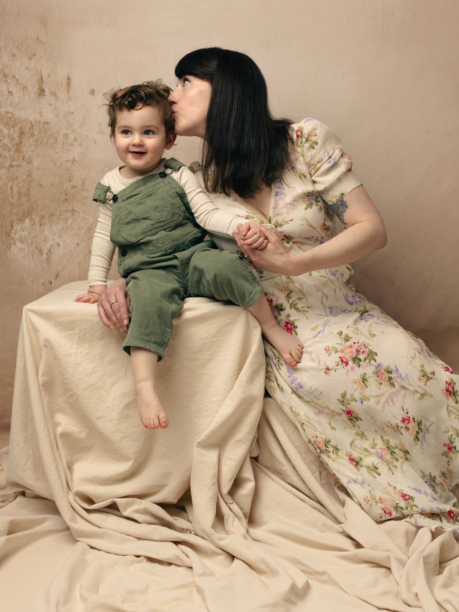 A series of four photos showing a child in green clothing rolling and playing on cream-colored fabric with floral patterns.