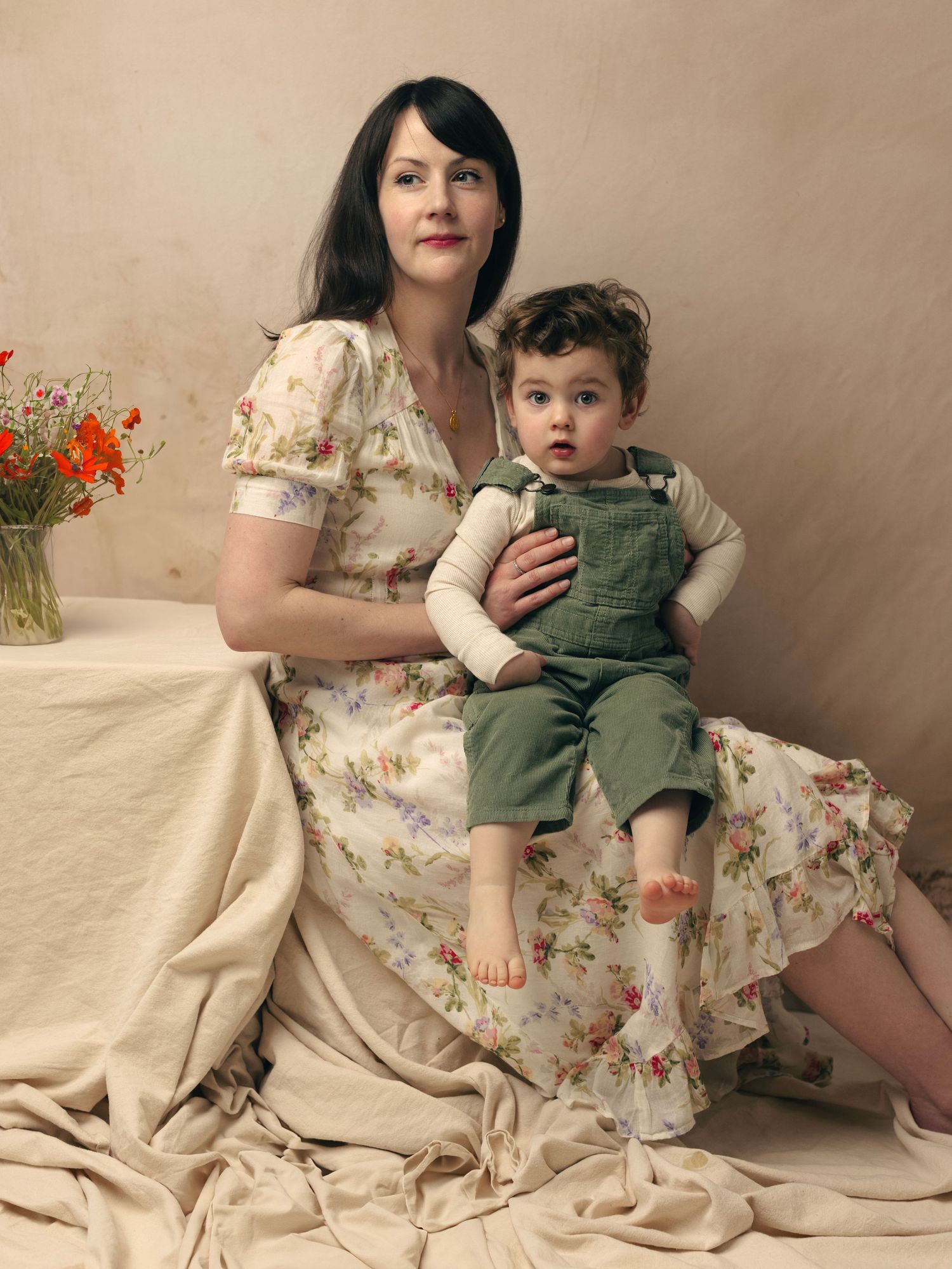 A series of five intimate portraits showing a parent and small child in overalls sitting together on beige fabric.