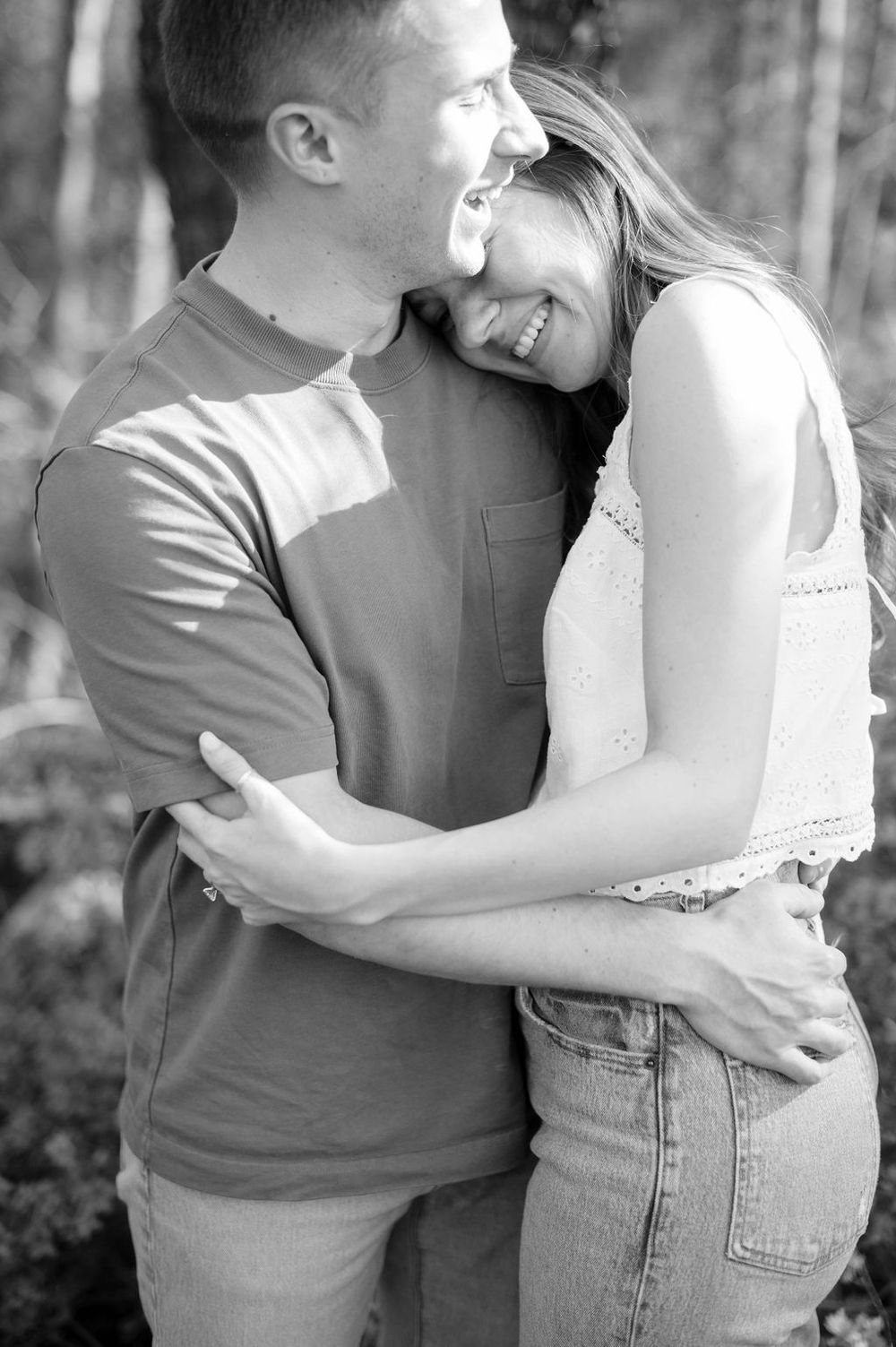 A candid black and white photo of a romantic couple embracing and laughing together outdoors.
