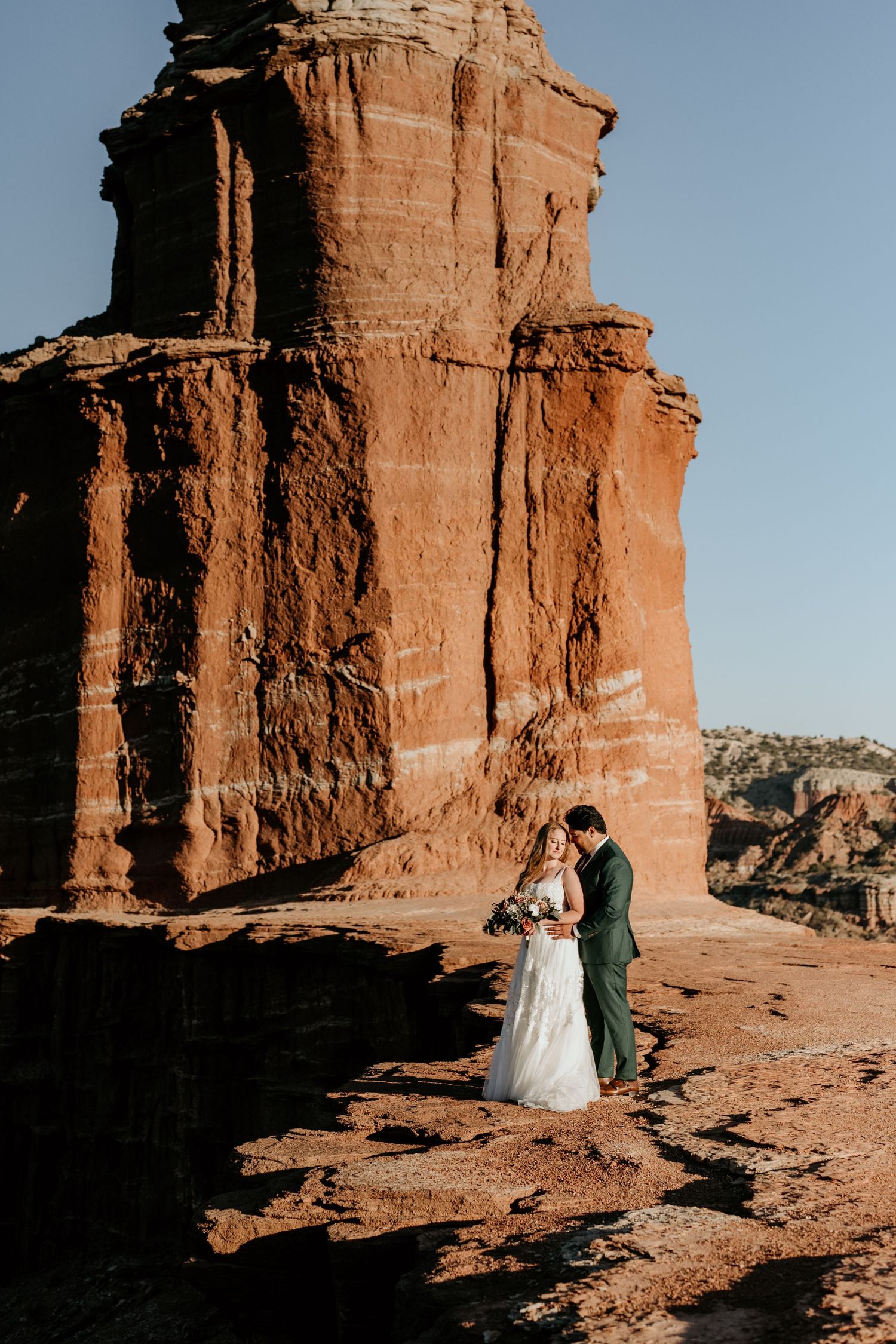 Desert wedding photos against dramatic red rock formations under blue sky.