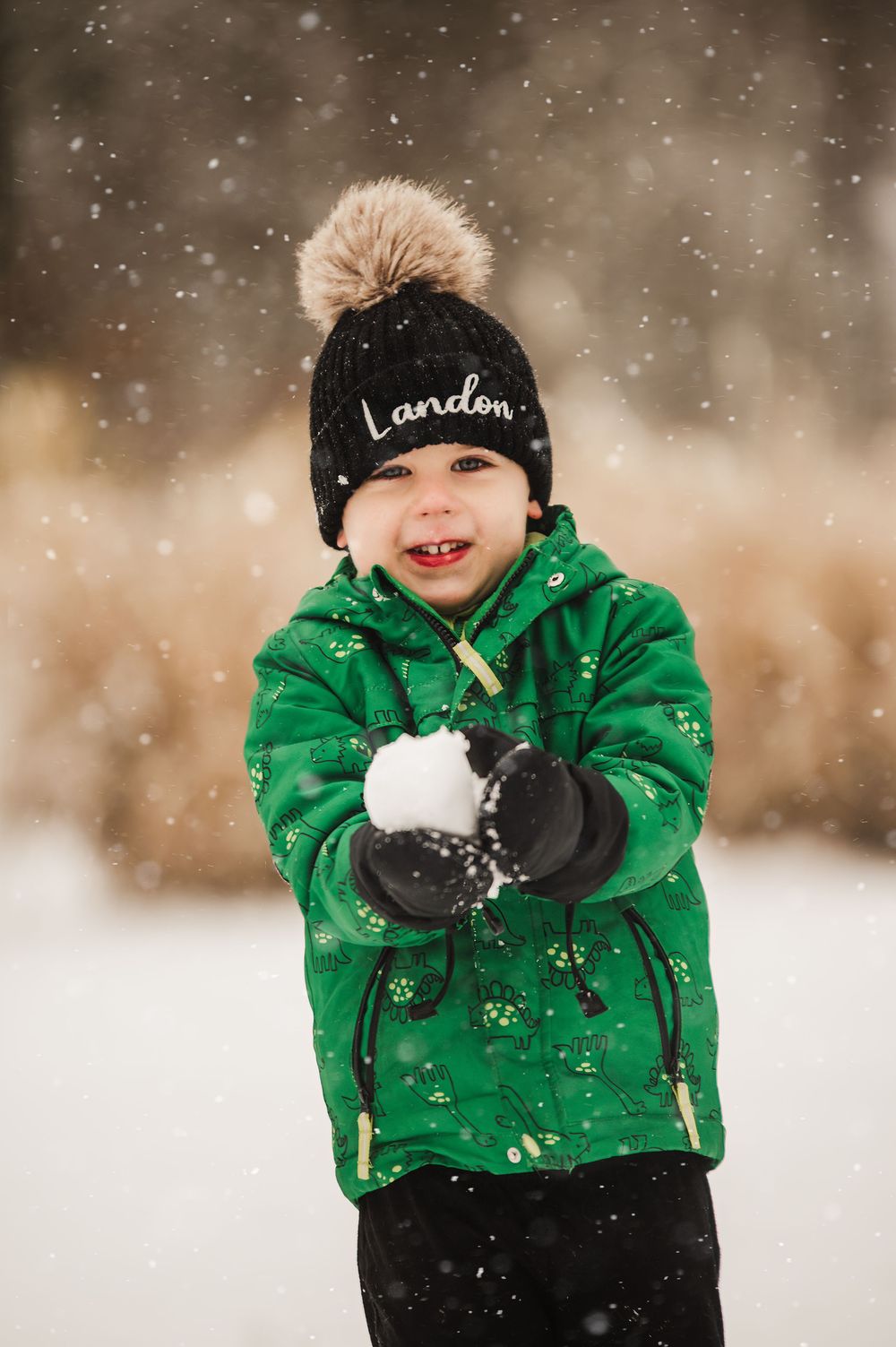 A child in a bright green winter coat and black hat plays with snow on a snowy winter day.