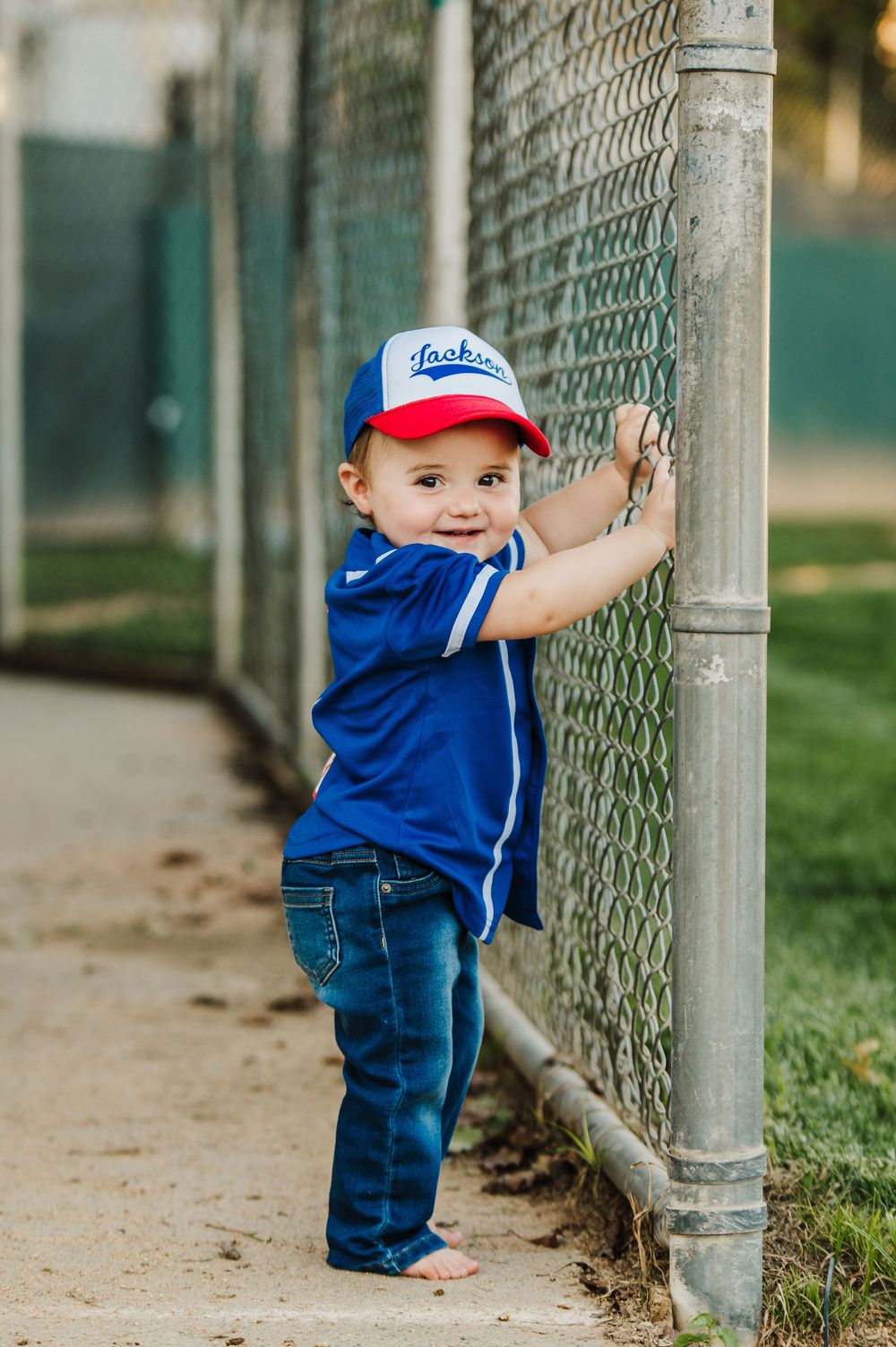 A toddler in blue overalls and baseball cap plays along a chain link fence in three sequential photos.