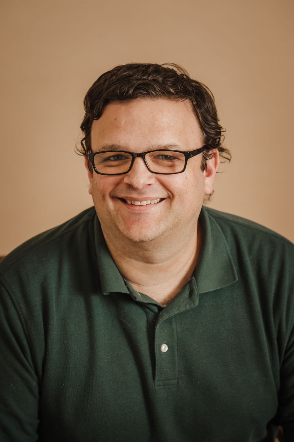 A series of five headshots showing someone in a green polo shirt and glasses with varying expressions and poses.