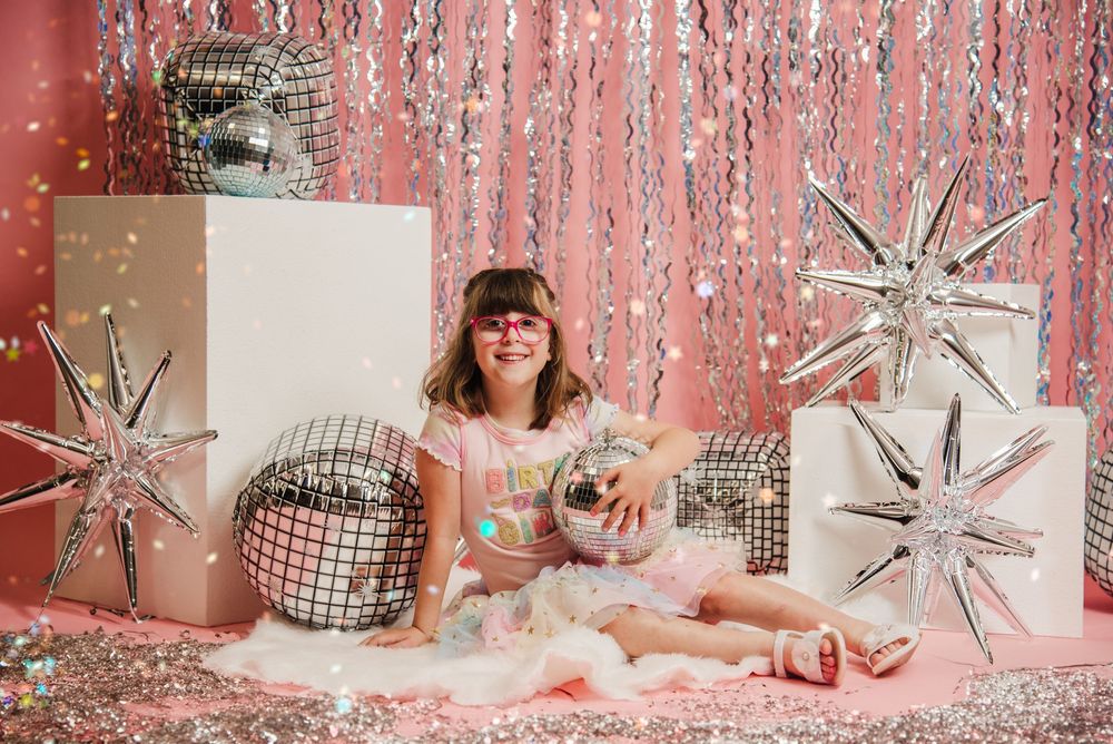 Decorative silver starburst ornaments and pink tinsel create a festive holiday backdrop for a winter photo session.