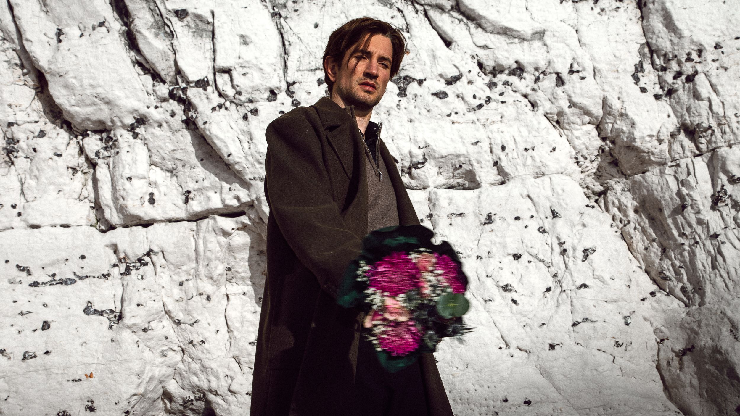 Person holding a vibrant pink bouquet against a white chalk cliff backdrop.