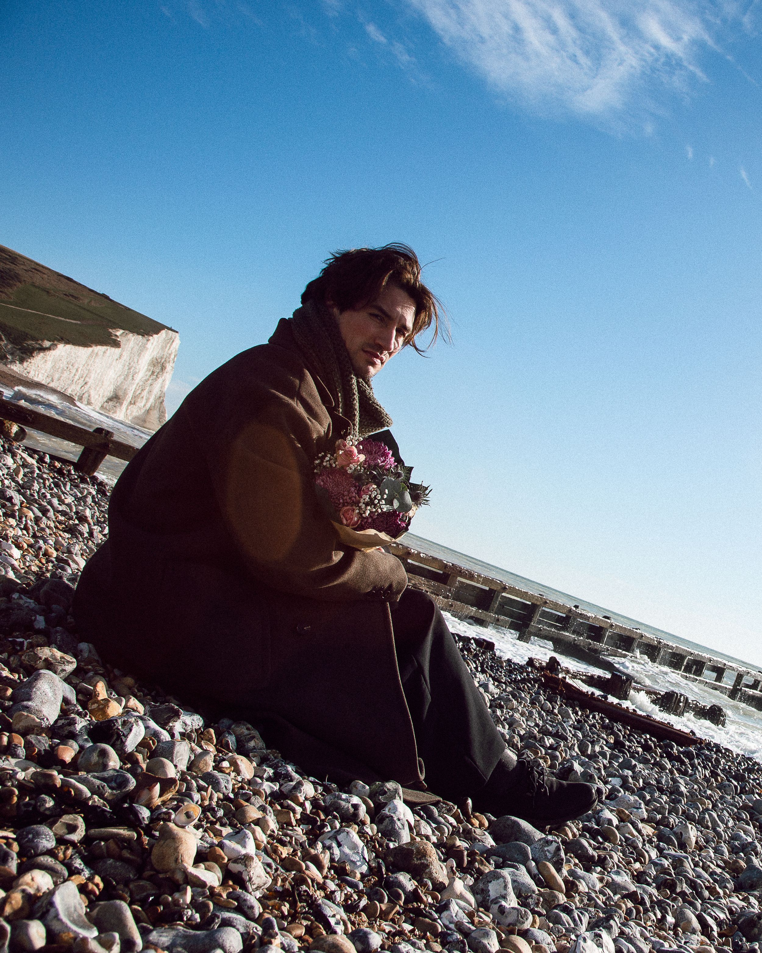 Person sitting on a rocky beach with blue sky in the background.