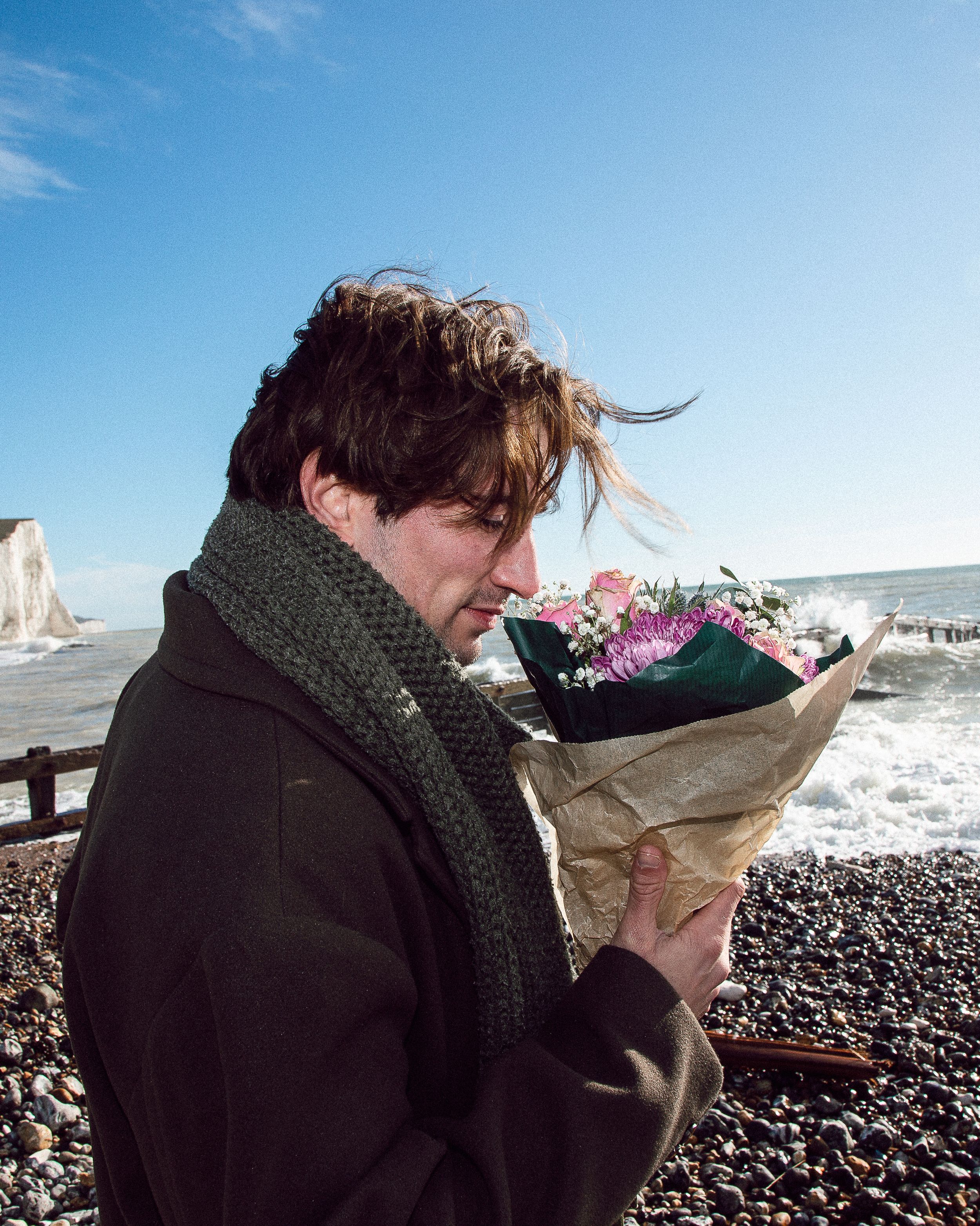 A sequence showing someone in a black coat reading a book on a windy beach with waves crashing in the background.