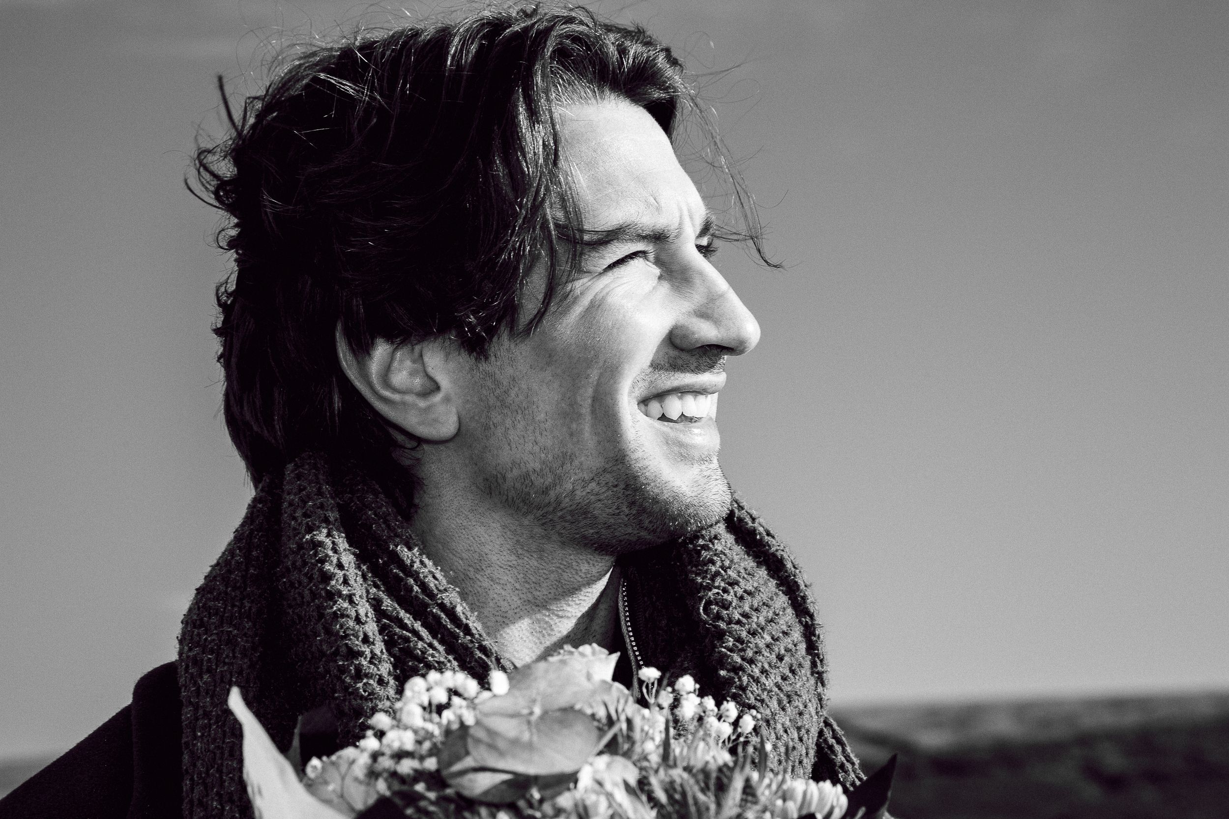 A black and white portrait of a person in a scarf holding flowers while smiling warmly.