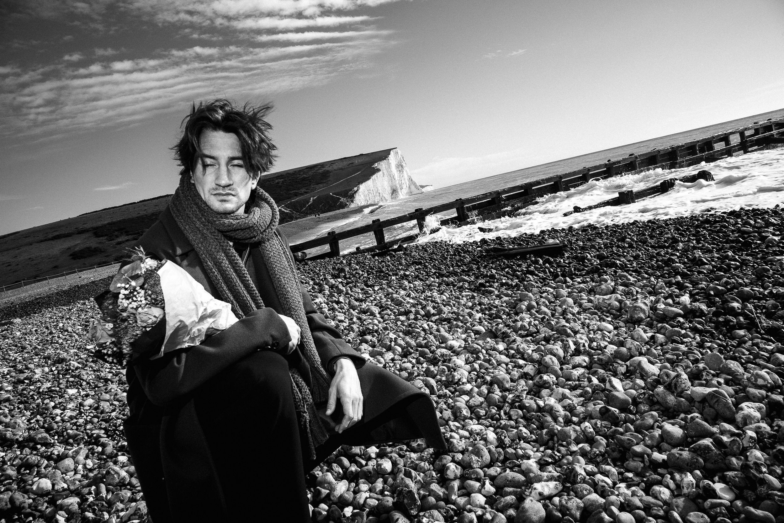 Dramatic black and white photo sequence of a person emerging from dark rocks on a beach at sunset.