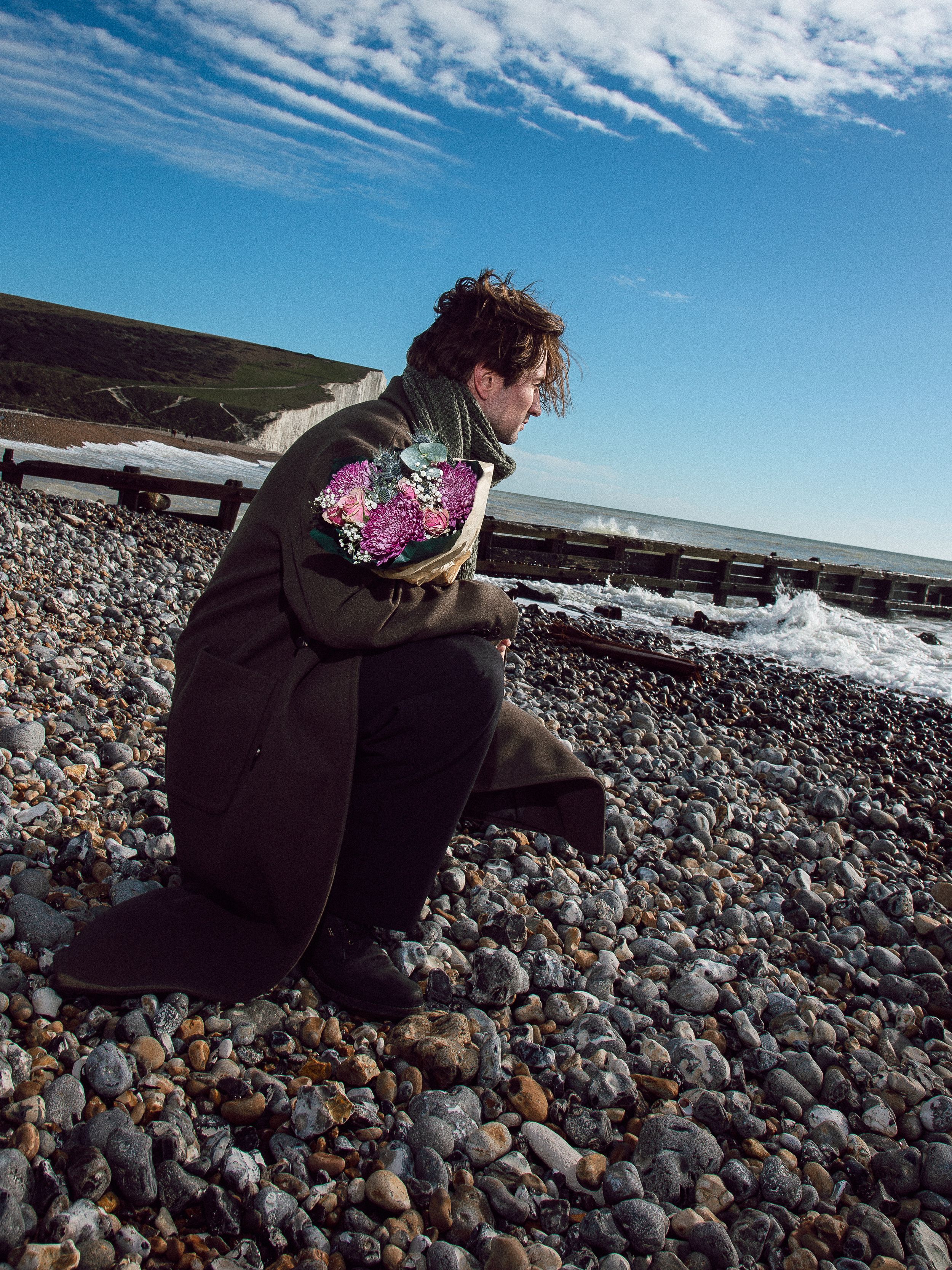 A sequence of photos showing someone collecting rocks on a pebbly beach under wispy clouds and blue skies.