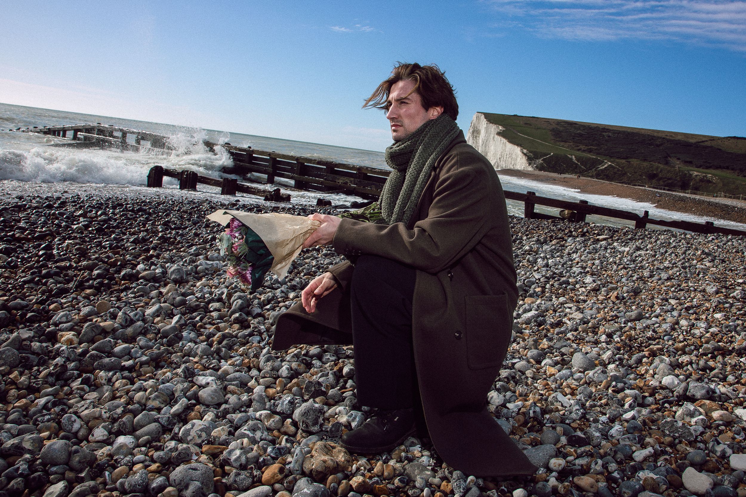 A sequence of images shows someone sitting on a rocky beach shore against a bright blue sky backdrop.