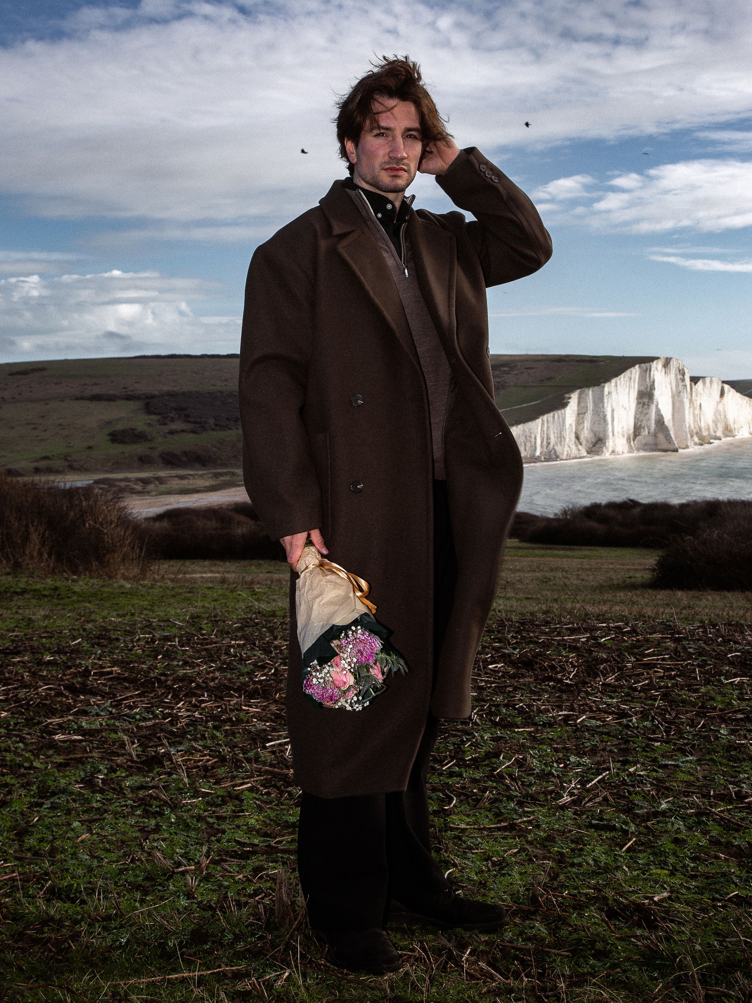 A figure stands against dramatic white cliffs and cloudy skies along England's southern coastline.