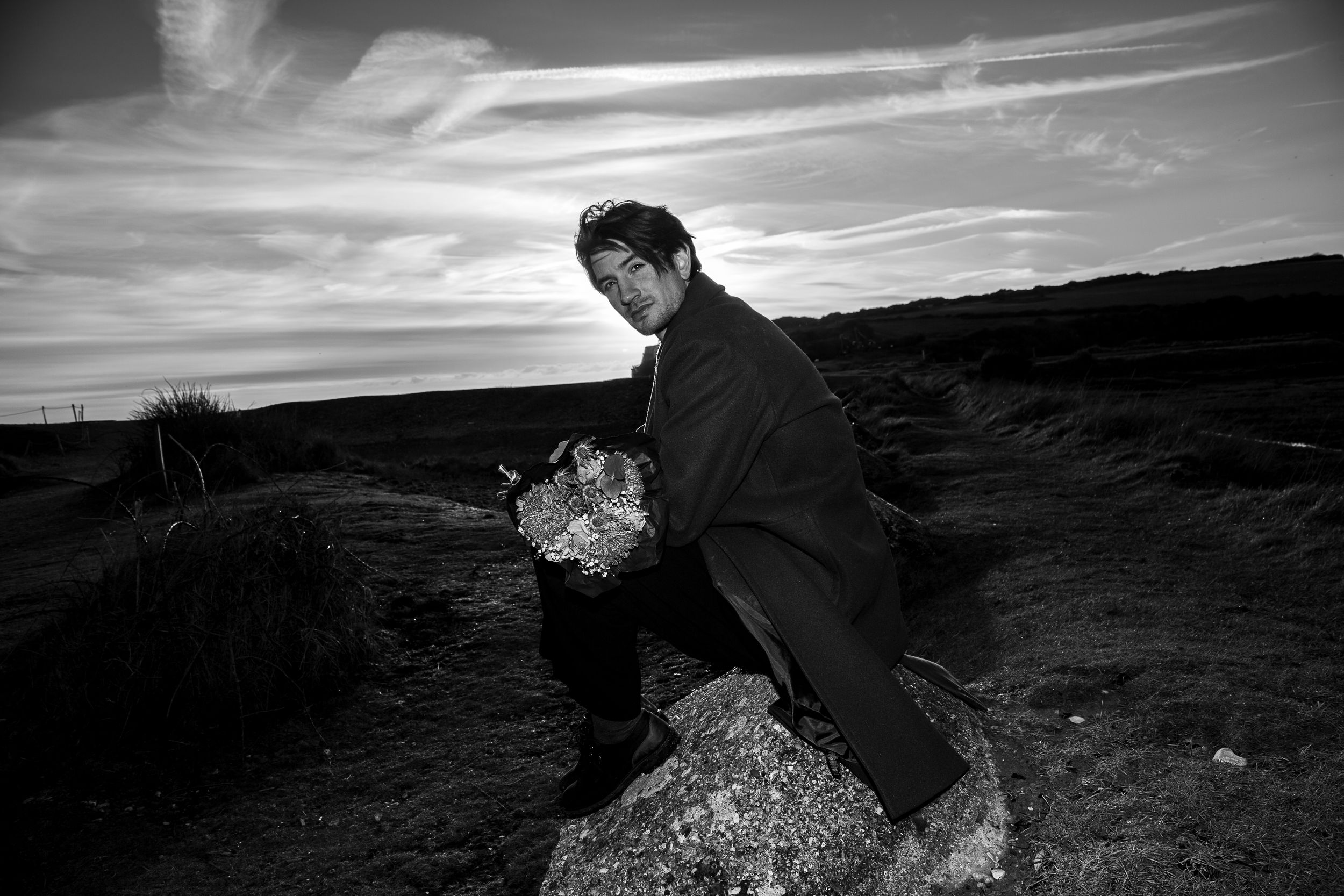 Black and white panoramic sequence shows a person walking and interacting with a rocky desert landscape at sunset.