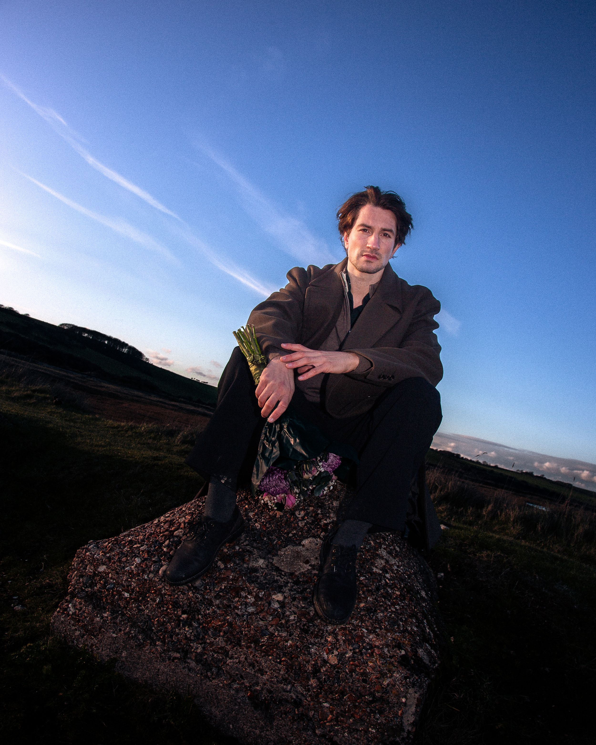 A figure sits on rocky terrain against a vibrant blue sky at sunset in a series of dramatic outdoor portraits.