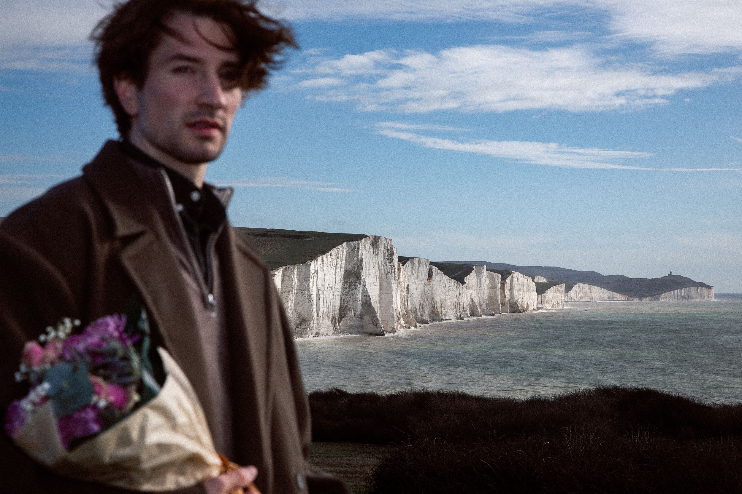 A scenic view of white chalk cliffs along the coastline with blue sky and wispy clouds above.