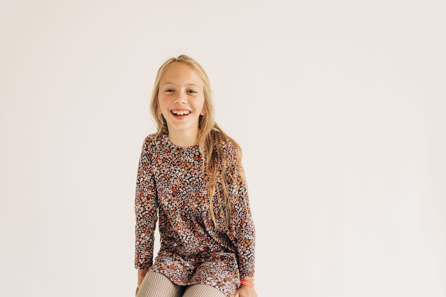 Young girl with floral shirt smiling with a white background.