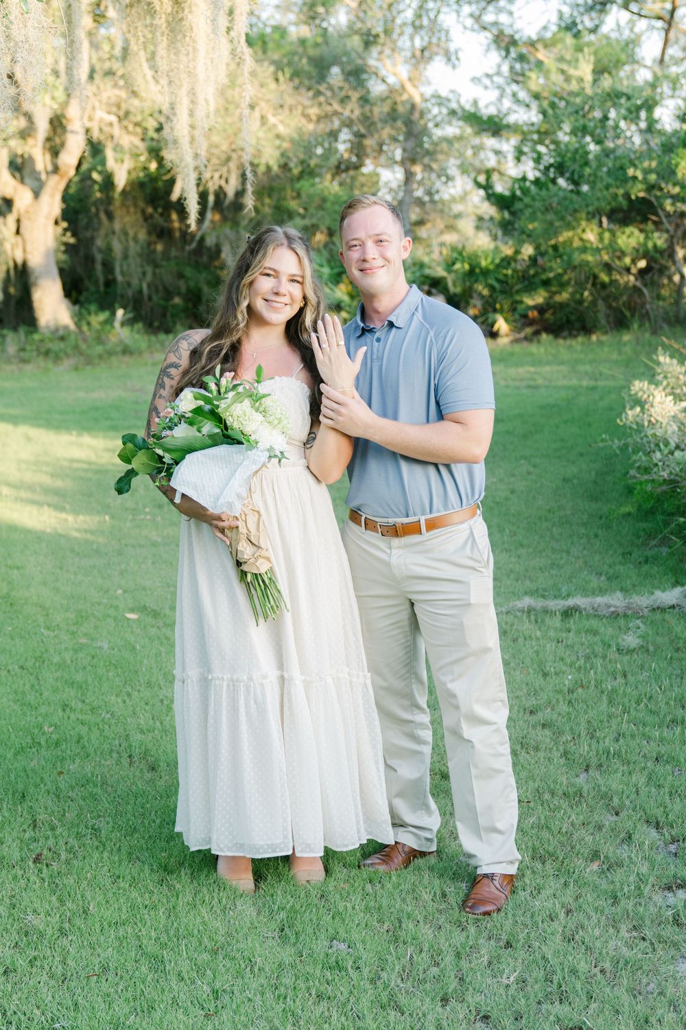 Couple engaged and smiling at the photographer on Jekyll Island Georgia, happily showing the ring