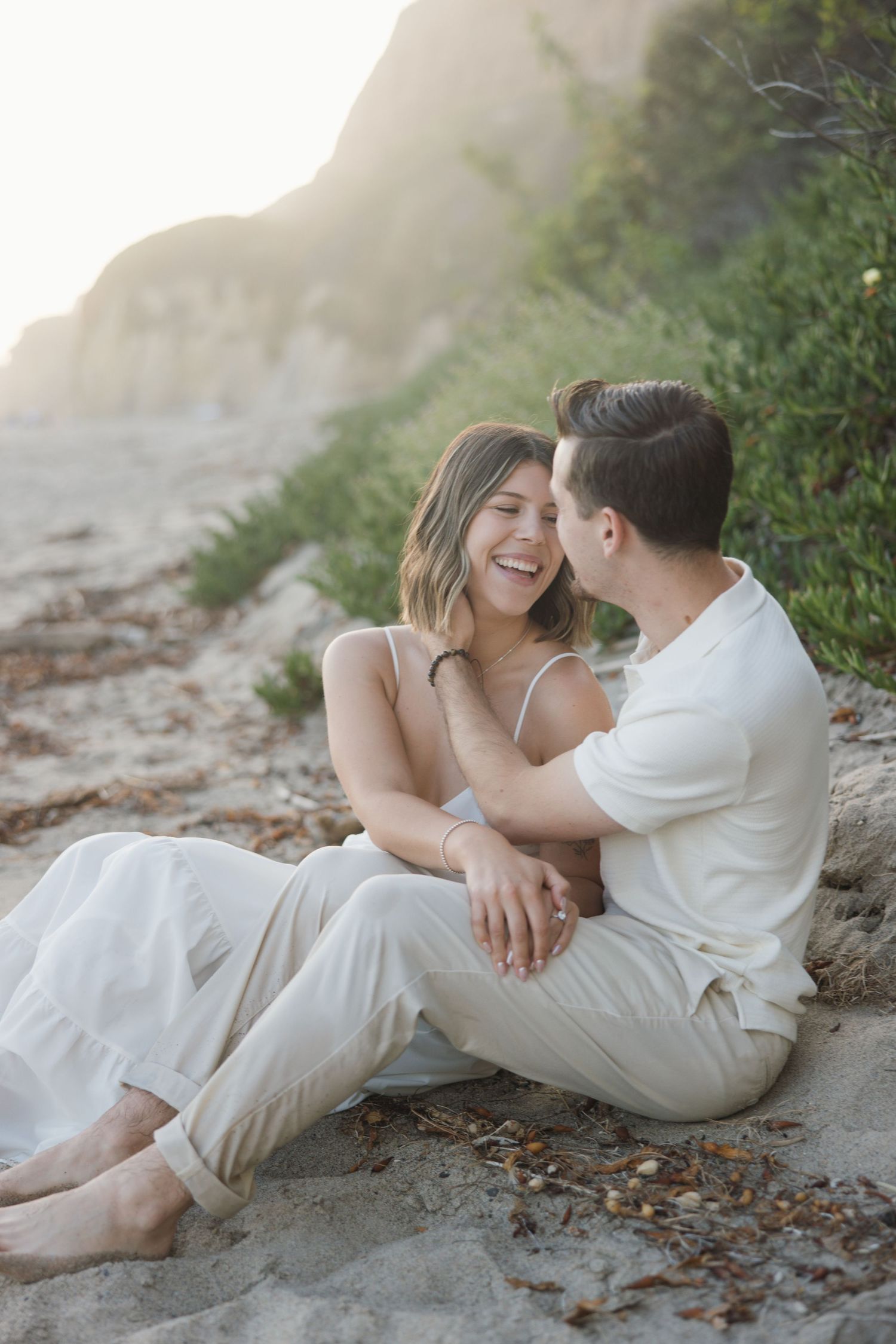Malibu engagement session at El Matador with a couple sitting on the beach laughing together