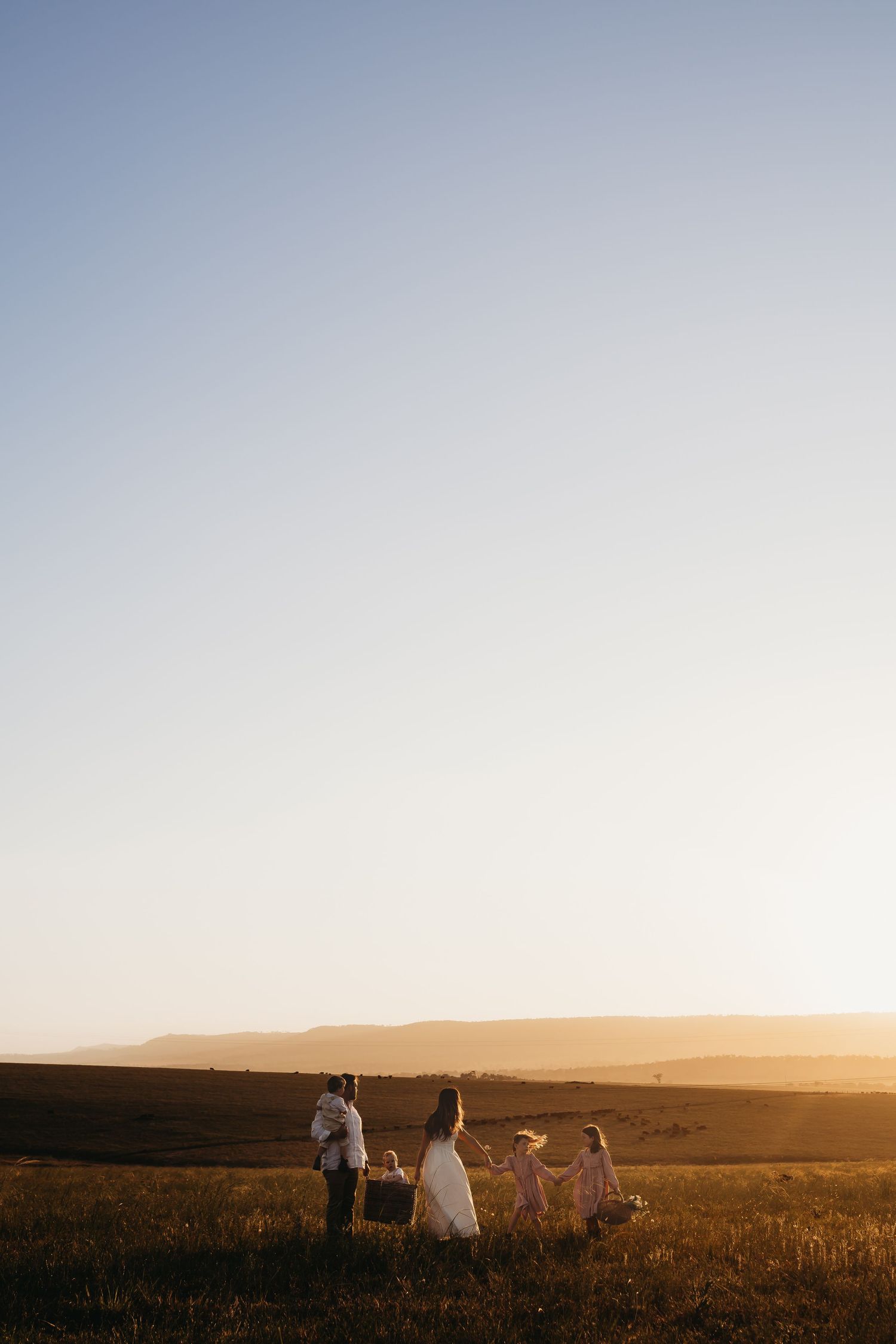 Silhouettes of people walking across a golden field at sunset with warm glowing light in the background.