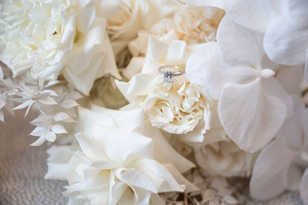Diamond engagement ring nestled among white roses and hydrangeas in bridal bouquet.