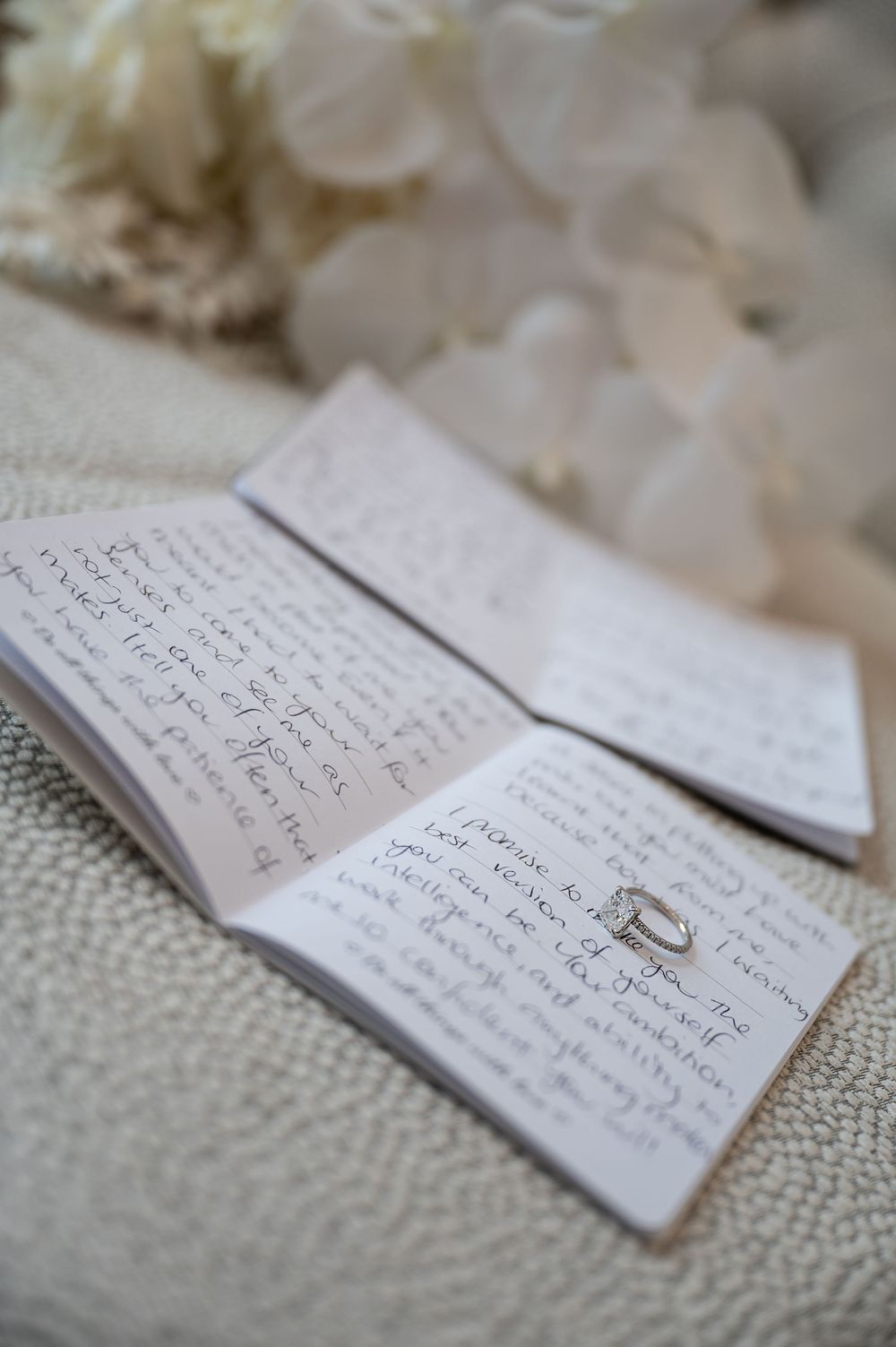Handwritten wedding vows with diamond engagement ring on white textured surface.