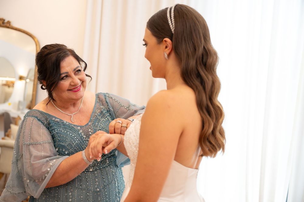 Mother helping bride with wedding dress details in a bright bridal suite before the ceremony.