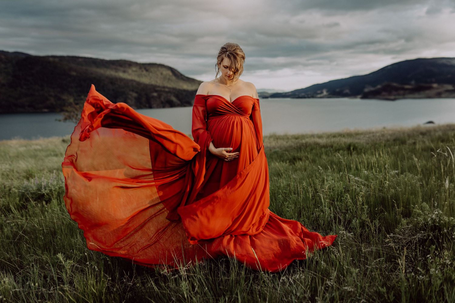 A flowing red dress creates dramatic movement against a misty mountain landscape at sunset.