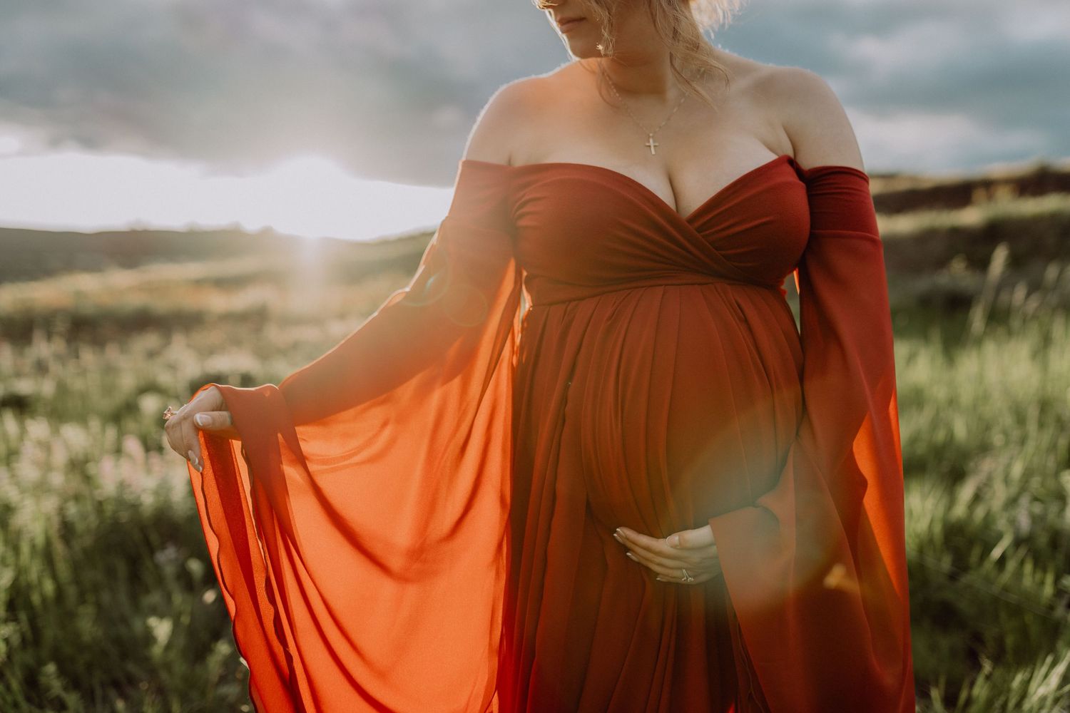 A flowing orange dress billows in the wind against a scenic natural landscape at golden hour.
