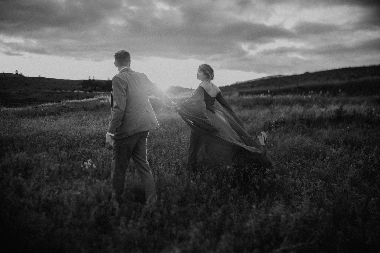 A black and white panoramic series showing people walking through a grassy hillside landscape at sunset.