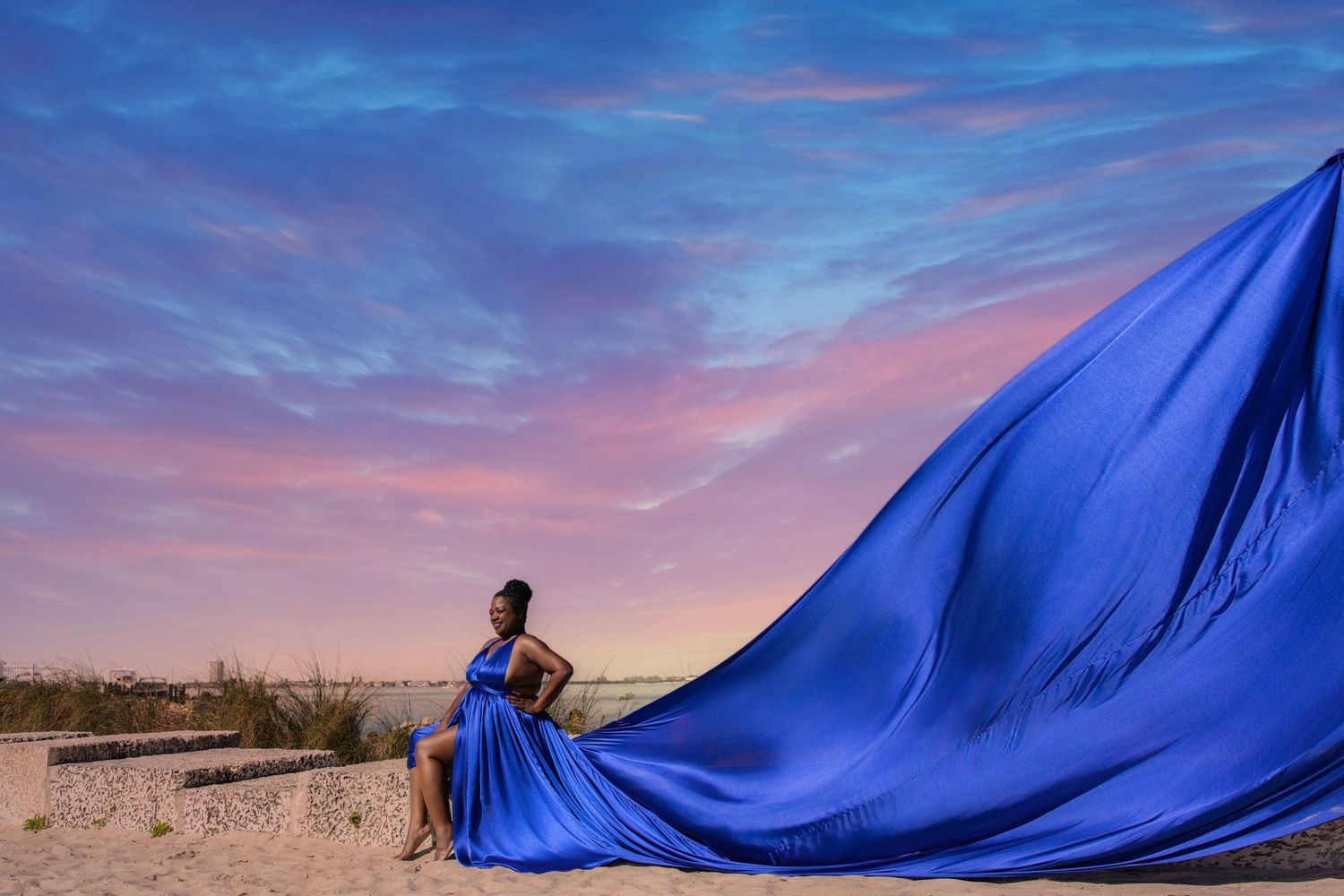 A large blue tarp billows dramatically against a vibrant sunset sky with pink and purple clouds. Flying dress photography