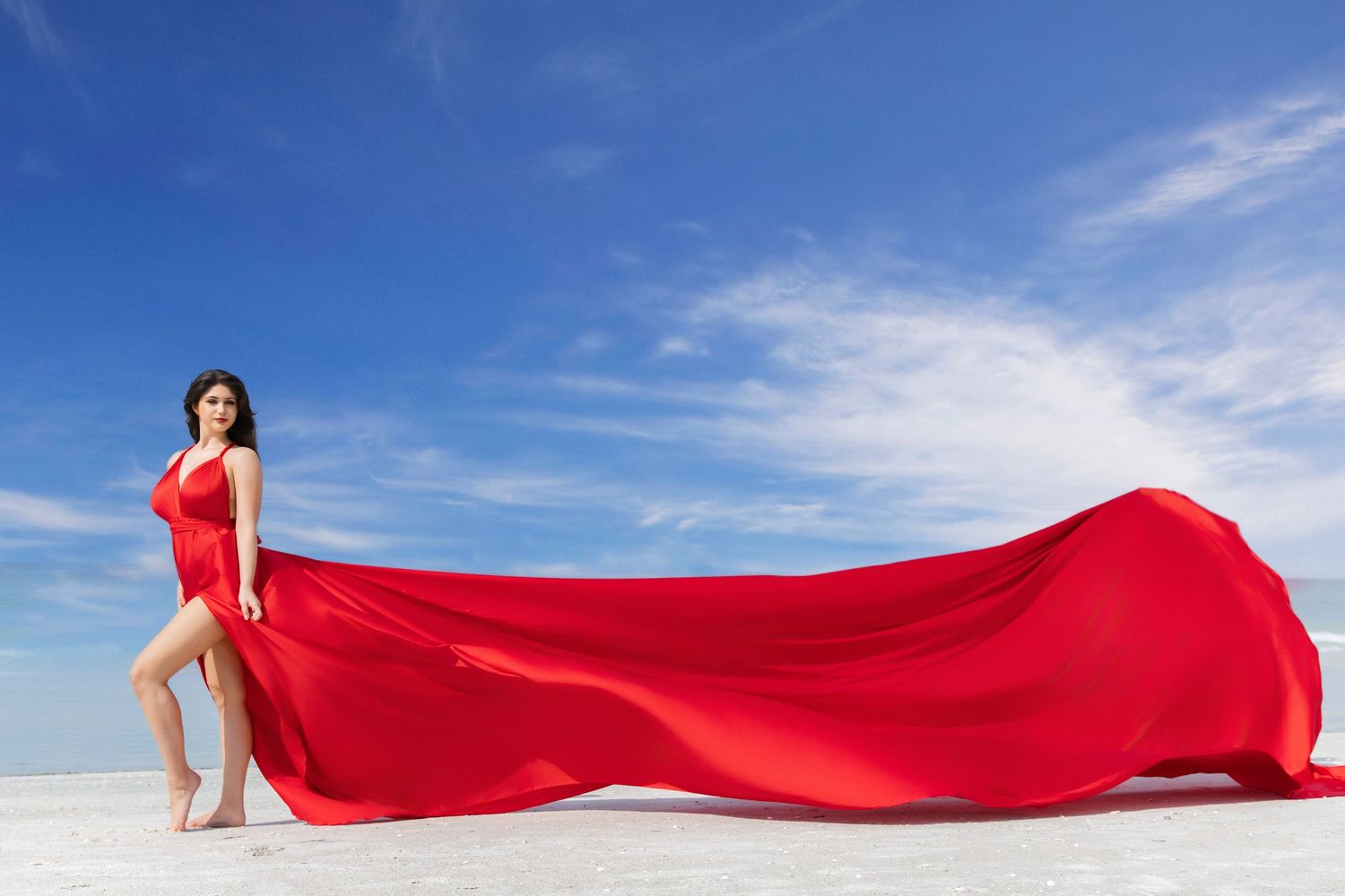 A flowing red fabric billows gracefully against a bright blue sky with white clouds.