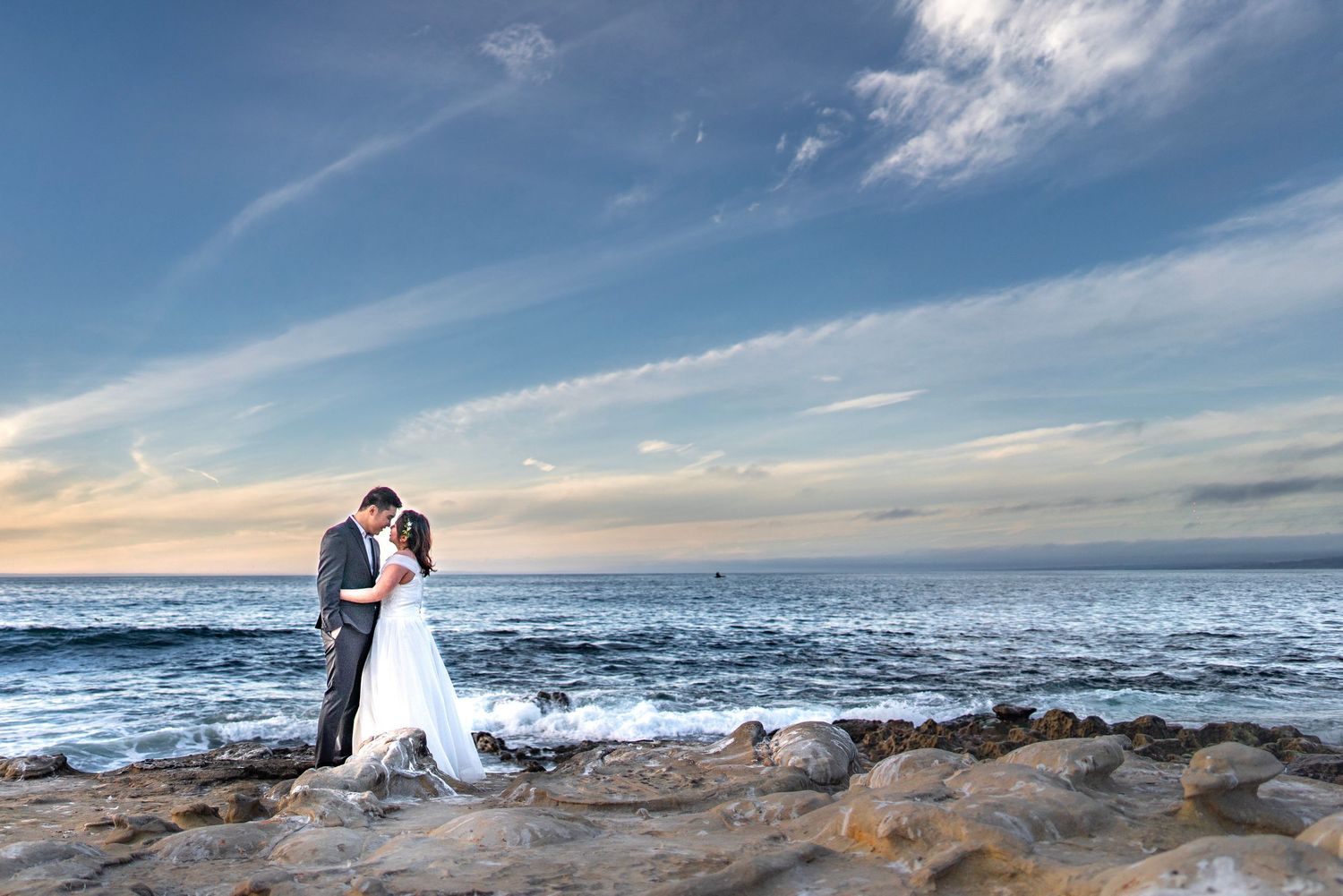 Scenic coastal wedding photos captured at sunset along a rocky beach with dramatic ocean and sky views.