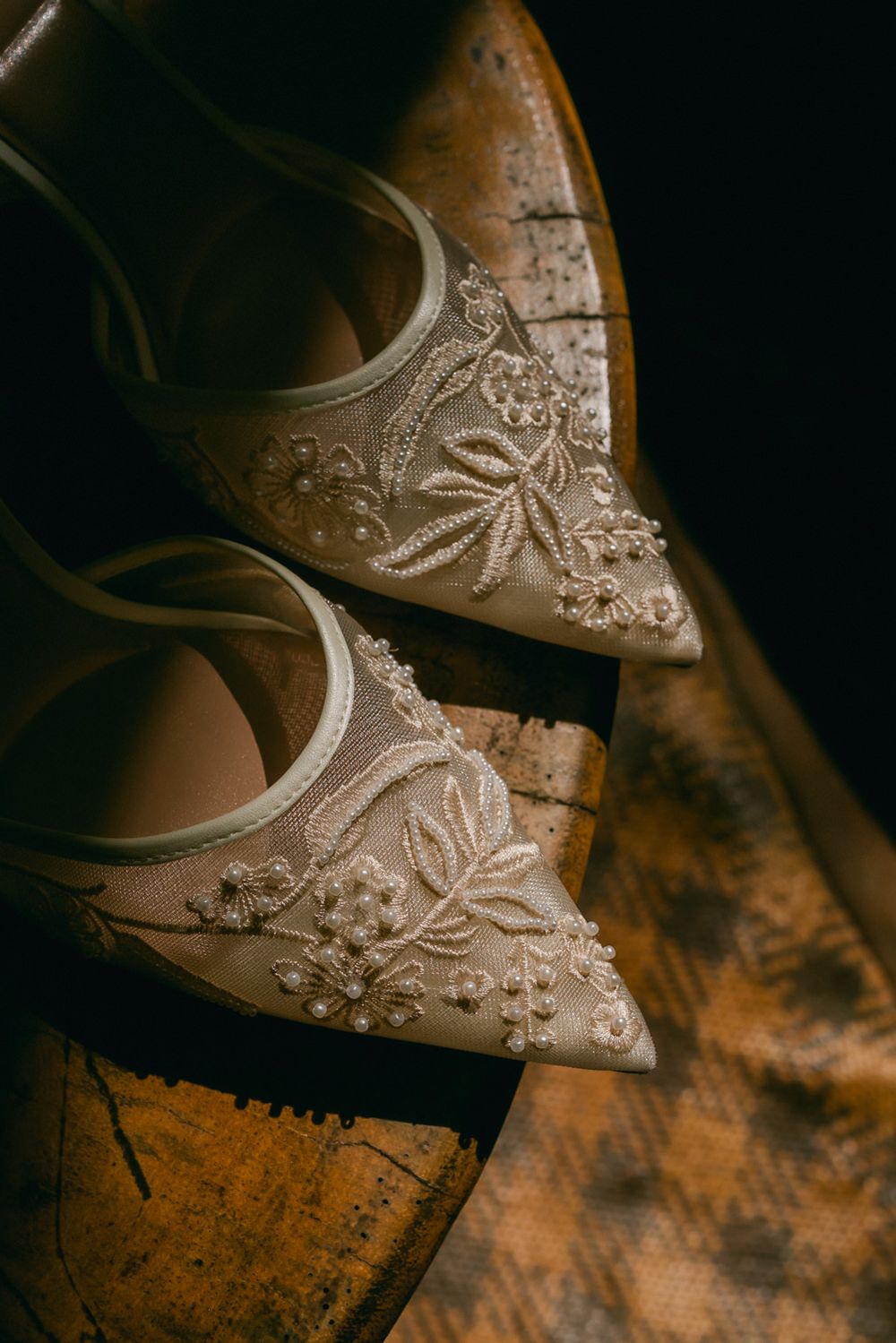 Close-up detail of an ornate lace pattern on a white bridal shoe against a dark background.