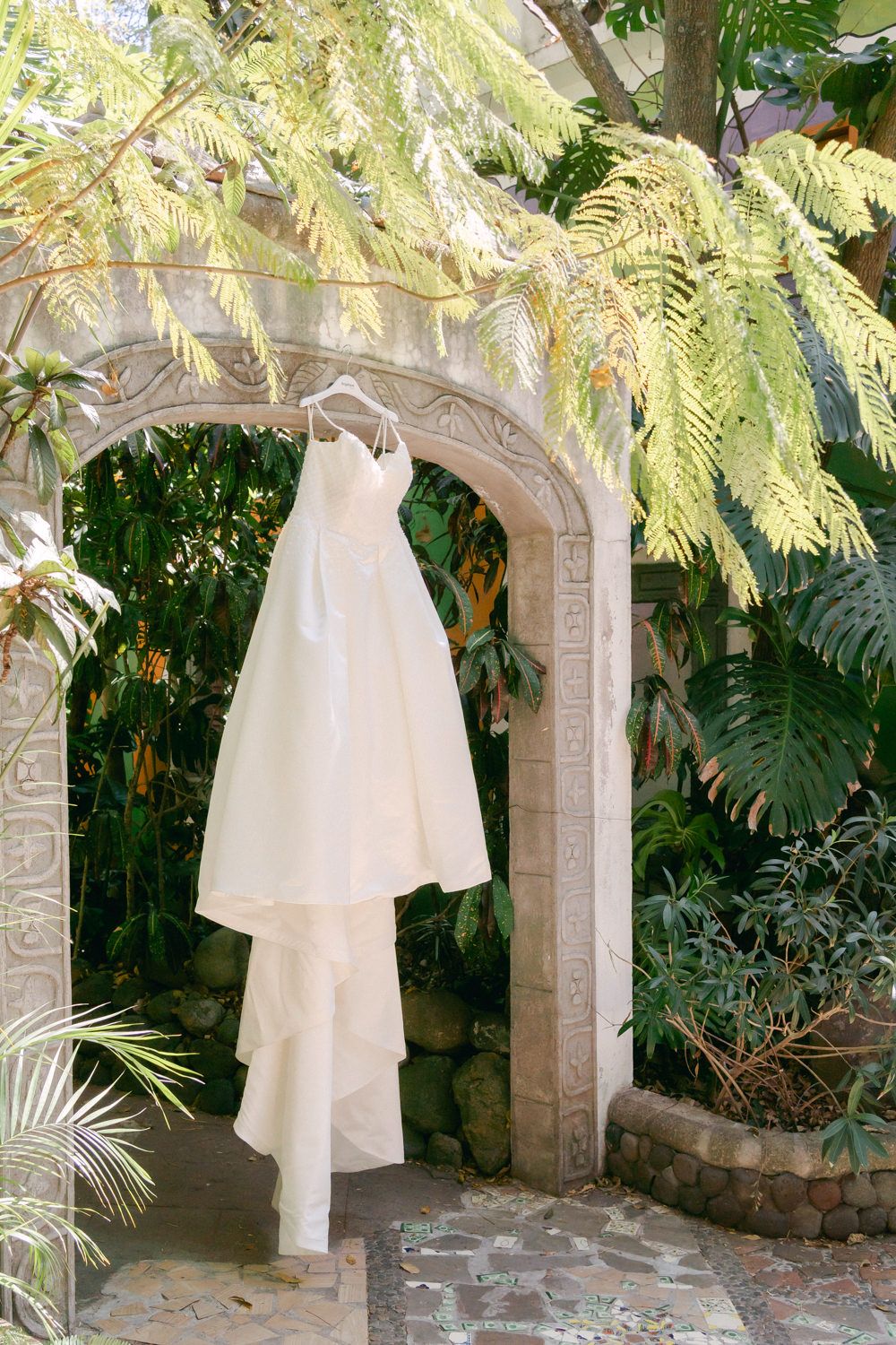 White flowing fabric draped between stone pillars in a lush tropical garden setting.