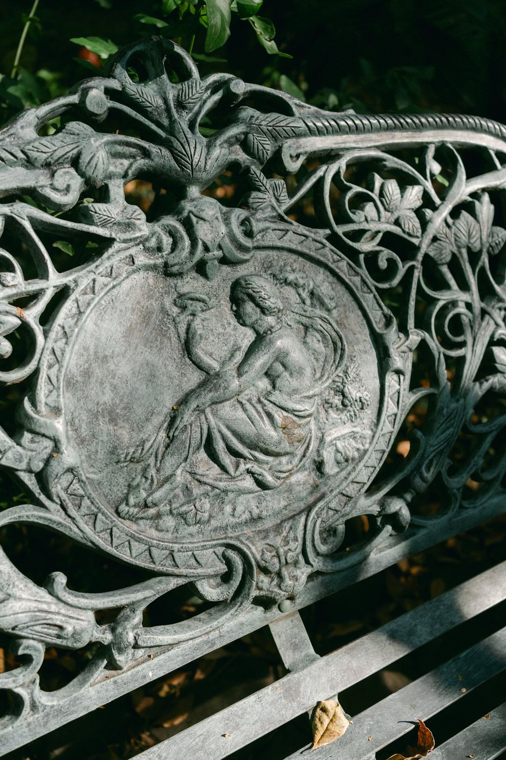 Ornate vintage metal bench detail showing decorative medallion with classical figure surrounded by scrollwork designs.