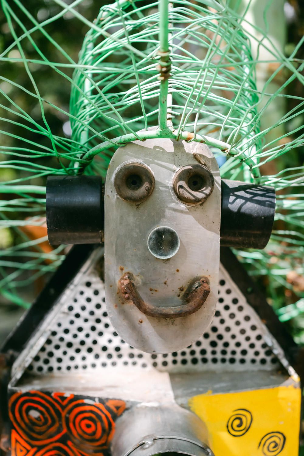 A whimsical robot face decoration made from metal parts with a perforated base and yellow accent designs.