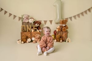A cozy first birthday setup with teddy bears, wooden crates, and triangle bunting decorations against a cream wall.