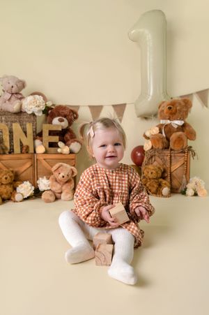 A collection of photos showing a baby in red plaid sitting with teddy bears and stuffed animals on a beige backdrop.