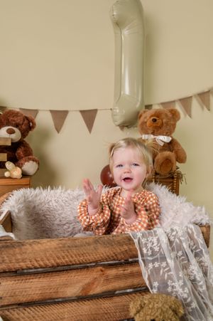 A child peeks over a rustic wooden bench with teddy bears and bunting decorations in the background.