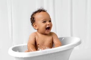 Happy baby taking a bath in a white bathtub with joyful expression.