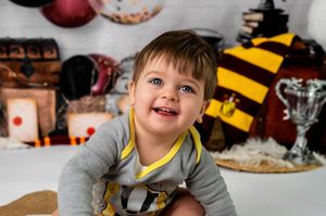 A joyful child wearing a gray sweater poses in front of holiday decorations and a striped scarf.